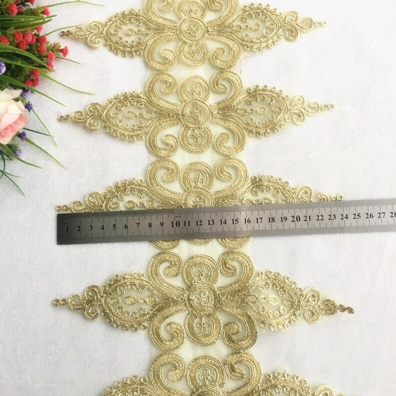 K&ouml;nnte beinhalten: Goldene Spitzenborte mit einem zarten Blumenmuster. Die Borte ist etwa 71 cm lang und zeigt ein sich wiederholendes Muster aus filigranen Spiralen und Blumen.