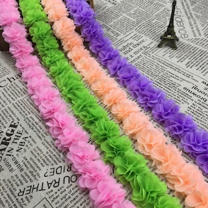 Può includere: Primo piano di cinque file di passamaneria in tessuto con forme di fiori arricciati. La passamaneria è in tonalità di rosa, verde, pesca e viola.