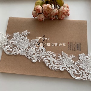 May include: White lace trim featuring a floral design. The lace is delicate and intricate, with small flowers and leaves. The trim is ideal for adding a touch of elegance to any project.