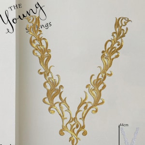 Könnte beinhalten: Eine V-förmige, goldfarbene Stickapplikation mit komplexen, geschwungenen Rankenmustern. Das Design ist symmetrisch mit einer spitzen Unterseite und zwei nach oben verlaufenden Zweigen. Ein kleiner Einschub zeigt eine weiße Version mit 44 cm Maß.