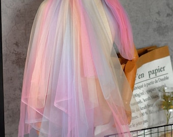 May include: Rainbow ombre tulle fabric with a soft, sheer texture. The fabric is draped over a dress form and has a layered, flowing look.