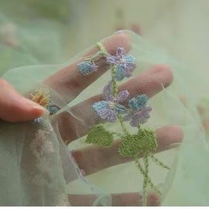May include: Green tulle fabric with embroidered flowers in shades of purple, blue, and green.