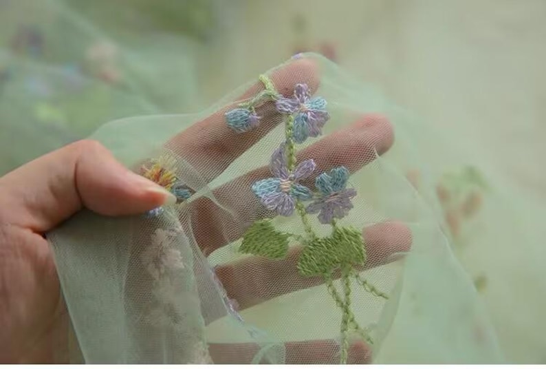 May include: Green tulle fabric with embroidered flowers in shades of purple, blue, and green.