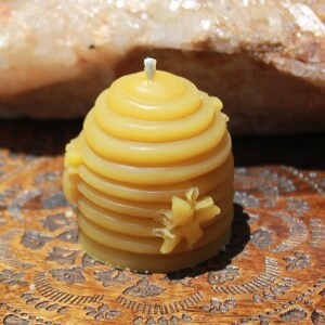 Puede incluir: Una pequeña vela de cera de abeja amarilla con forma de panal. La vela está sobre una bandeja de madera con un diseño tallado.