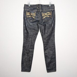 Peut inclure: Jean skinny bleu foncé avec des détails en fil de fer barbelé brodés en or sur les poches arrière.