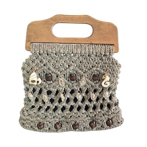 May include: A macrame handbag with a wooden handle. The bag is olive green with dark brown wooden beads and decorative charms. The charms include a seahorse and a heart. The bag has a woven design.