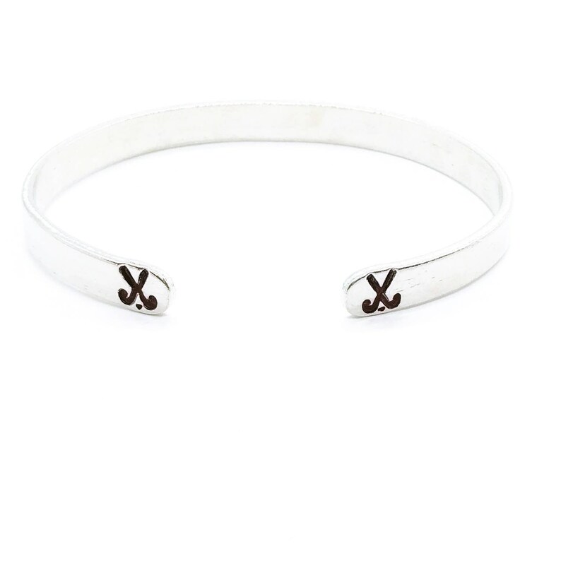 May include: A silver bangle bracelet with two hockey stick symbols engraved on the ends.