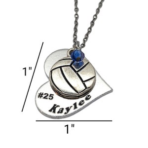 May include: Silver heart-shaped pendant necklace featuring a volleyball charm and a blue crystal. The pendant is engraved with the text "#25 Kaylee" and measures 2.5 cm in diameter.