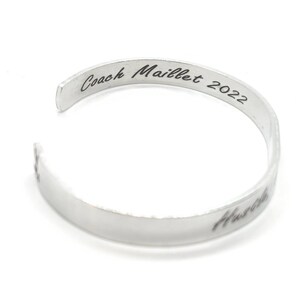 May include: Silver metal bracelet inscribed with "Coach Maillet 2022" on the top and "Hustle" on the bottom.