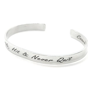 May include: Silver bangle bracelet with the inscription "Hit & Never Quit" and "Coach" on the back.