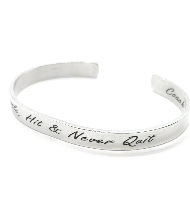 May include: Silver bangle bracelet with the inscription "Hit & Never Quit" and "Coach" on the back.