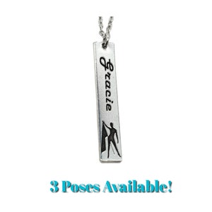 May include: Silver necklace with a vertical bar pendant. The pendant has the name "Gracie" engraved on it and a silhouette of a person holding a flag.