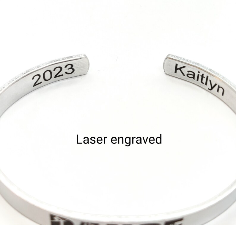 May include: Silver bangle bracelet with laser engraved text "Kaitlyn" and "2023".