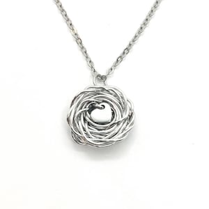 May include: A silver necklace with a pendant shaped like a nest with a heart in the center.