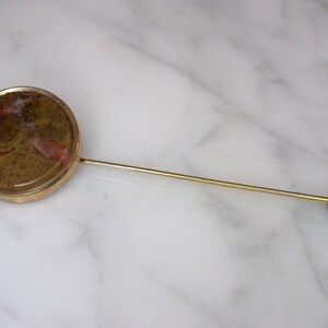 May include: A gold-toned tie tack with a round, brown agate stone with red and white swirls.