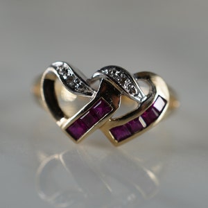 May include: A gold ring with two intertwined hearts. The hearts are set with red rubies and white diamonds.