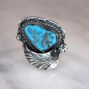 May include: A silver ring with a turquoise stone set in a detailed design. The stone is a light blue color and has a rough, natural texture.