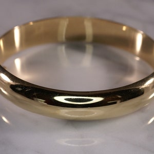 May include: A gold bangle bracelet with a smooth, rounded surface.