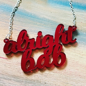 May include: A red acrylic necklace with the words "alright babe" in a cursive font.