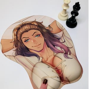 May include: A 3D mouse pad featuring an anime-style illustration of a character with lion ears, green eyes, and long brown hair. The character wears a white lace-up top. A white chess queen and a black chess king are positioned near the mouse pad.
