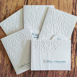 May include: Five white greeting cards with embossed tree designs. The cards have different tree designs and the text "With Deepest Sympathy" and "With Sympathy" printed on them.