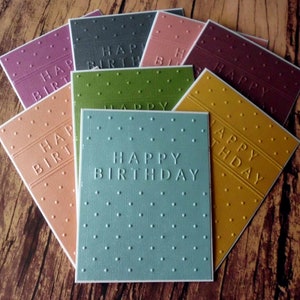 May include: A set of nine greeting cards with different colored backgrounds and embossed textures. Each card says "Happy Birthday" in a white font.