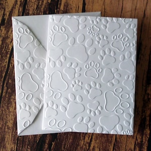 May include: White card with a raised paw print pattern. The card is folded in half and has a white envelope.