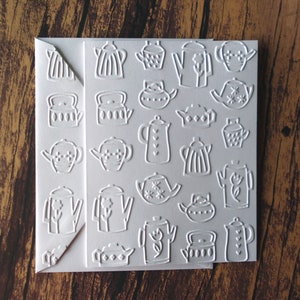 May include: White card with an embossed pattern of various teapots and kettles. The card is folded in half.