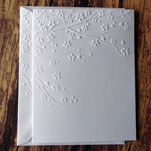 May include: A white card with a raised embossed design of a branch with small flowers. The design is in the upper right corner of the card.