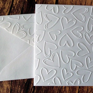 May include: A white card with a raised design of hearts. The card is blank and ready for writing.