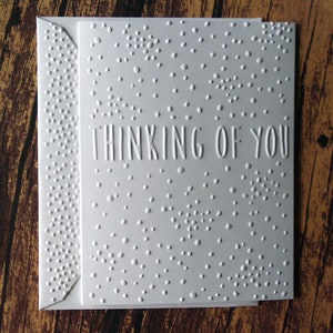 May include: White card with a textured pattern of small dots and the text "Thinking of You" in a bold, sans-serif font.