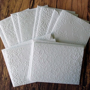 May include: A stack of white embossed cards with various floral patterns. The cards are blank and perfect for writing notes or messages.