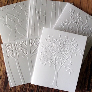 May include: Set of five white embossed cards with different nature-themed designs. The designs include a tree with leaves, a tree with birds, and a tree with branches.