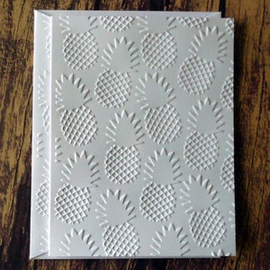 May include: White card with a raised embossed pattern of pineapples. The pineapples are in a repeating pattern.