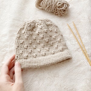 baby hat knitting pattern with wrapped bobble stitch. sandy beige hat with soft cream blanket background.