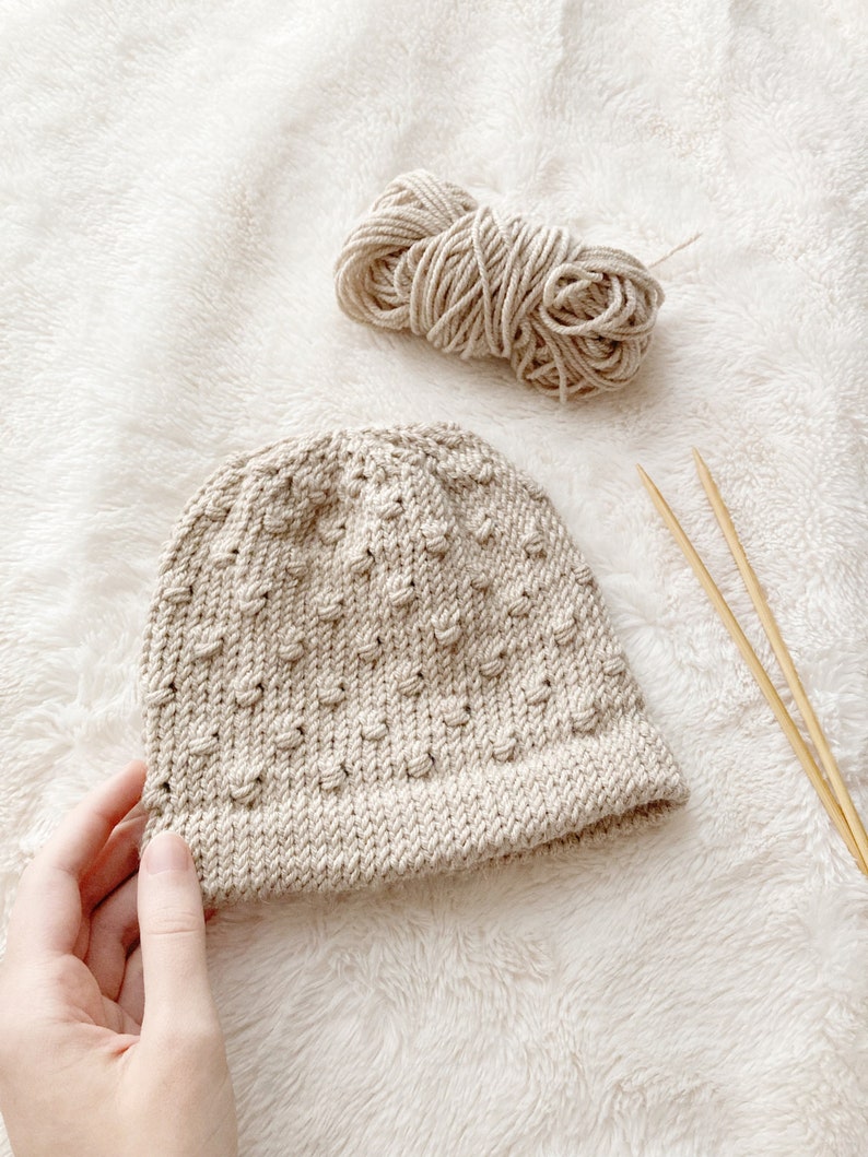baby hat knitting pattern with wrapped bobble stitch. sandy beige hat with soft cream blanket background.