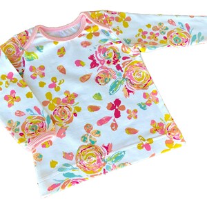 May include: White long-sleeved shirt with a pink floral print. The shirt has a pink trim around the neckline and cuffs.