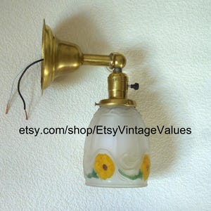 May include: Vintage brass wall sconce with a frosted glass shade. The shade features yellow floral designs and green leaves. The sconce has exposed wiring and the text "etsy.com/shop/EtsyVintageValues".