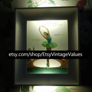 May include: A framed, illuminated artwork featuring a ballerina in a green tutu and teal top, poised on a bridge. The artwork is set within a white, square frame, with the text "etsy.com/shop/EtsyVintageValues" at the bottom.