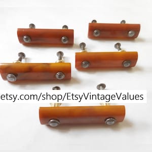 May include: Six vintage rectangular drawer pulls in shades of amber and brown. Each pull has two silver-toned rivets and a brass-colored screw. The pulls are arranged on a white background. Text: etsy.com/shop/EtsyVintageValues.