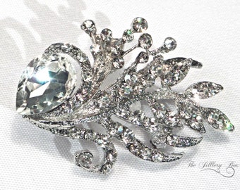 May include: A silver brooch with a large clear crystal and smaller crystals arranged in a floral design.