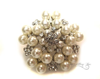 May include: A large, white pearl and rhinestone brooch in the shape of a flower. The brooch is made of silver tone metal and has a cluster of pearls in the center.
