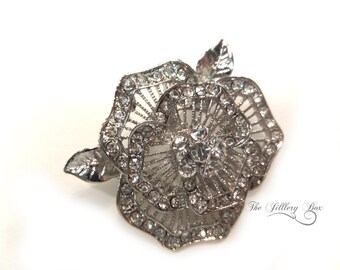 May include: A silver-toned rose brooch with clear rhinestones. The rose is made of metal and has a delicate, intricate design.