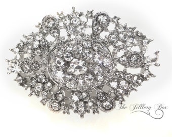 May include: A large, silver-toned brooch with a floral design. The brooch is covered in clear rhinestones of various sizes.