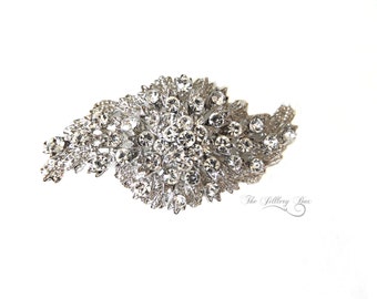May include: A silver-toned brooch with a large cluster of clear rhinestones in a floral design. The brooch has a delicate, intricate design and is perfect for adding a touch of sparkle to any outfit.