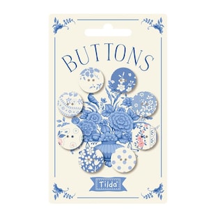May include: A set of seven round buttons arranged on a cream-coloured display card. The buttons feature various blue and white patterns, including floral, polka dot, and lace designs. The card displays the text BUTTONS and the brand name Tilda.
