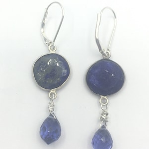 May include: A pair of silver dangle earrings with blue gemstone drops. The top of each earring features a round, blue lapis lazuli stone.