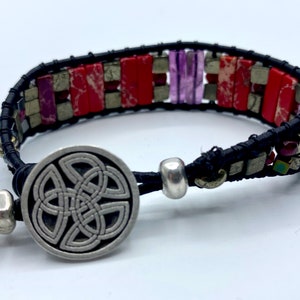 May include: A black leather bracelet with red, purple, and silver beads. The bracelet has a silver Celtic knot clasp.