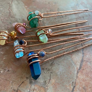 May include: A set of eight copper hair pins with various coloured crystal stones wrapped in copper wire. The stones include blue, green, pink, and yellow.