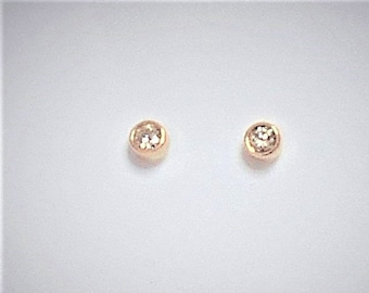 May include: A pair of small, round, gold stud earrings with a single clear stone in the center of each.